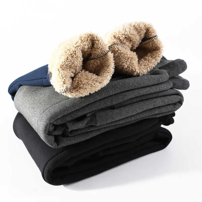 Stack of folded fleece pants in gray, black, and blue with fluffy brown trim on a white background
