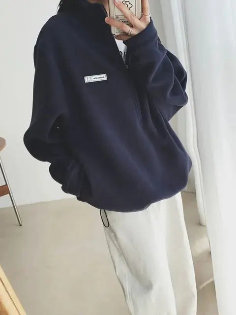 Person wearing a navy blue fleece sweater with a small logo on a white background