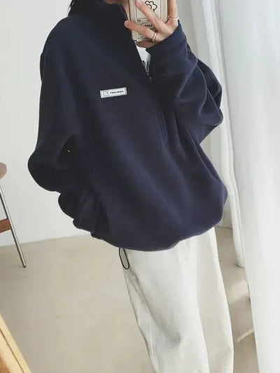 Person wearing a navy blue fleece sweater with a small logo on a white background