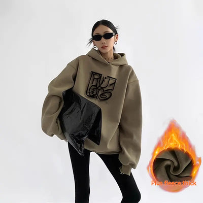 Person wearing a beige hoodie with a logo, holding a black bag, on a white background.