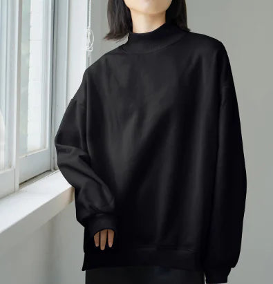 Person wearing a black sweatshirt standing in front of a window with white blinds.