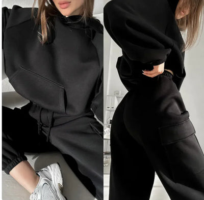 Person wearing a black outfit with a hoodie and pants, sitting on a couch.
