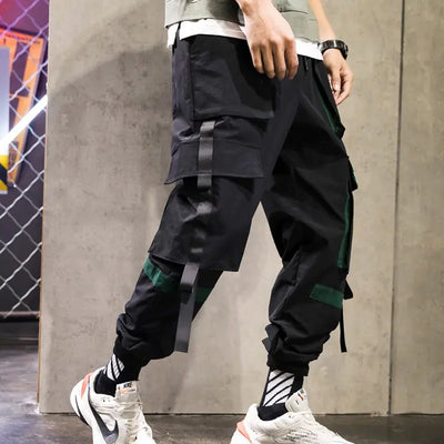 Person wearing black and green pants with white sneakers against a concrete wall.