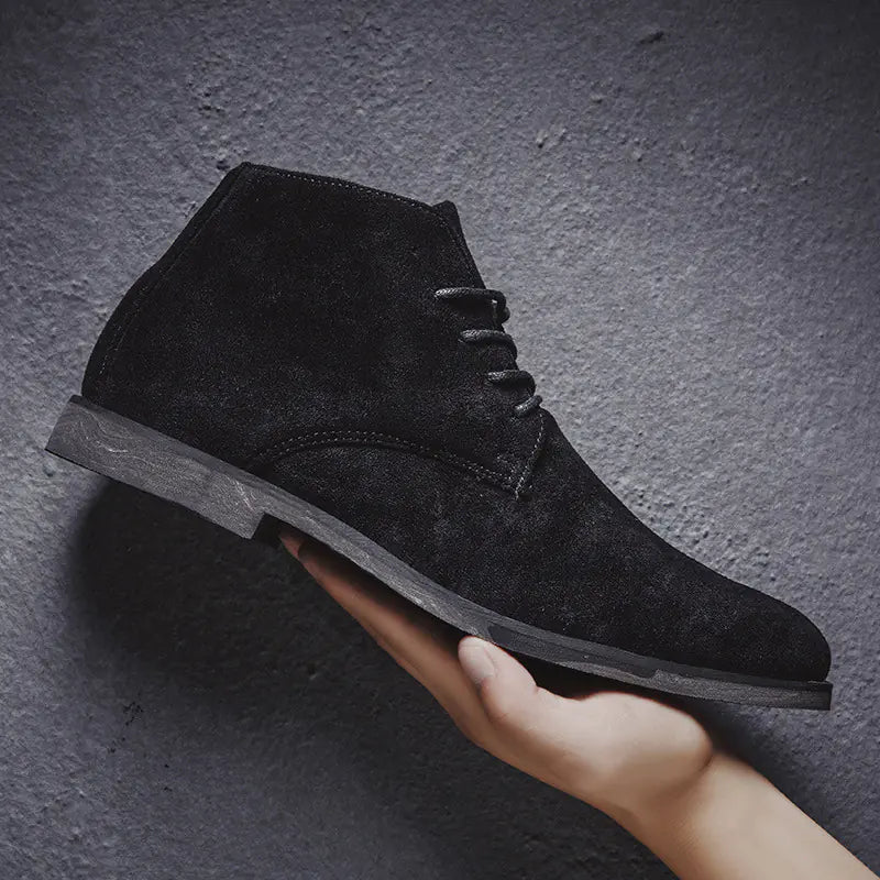 Black suede ankle boot held by a hand against a dark gray background