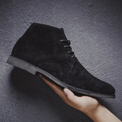 Black suede ankle boot held by a hand against a dark gray background