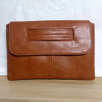 Brown leather clutch bag on a wooden surface with a white background