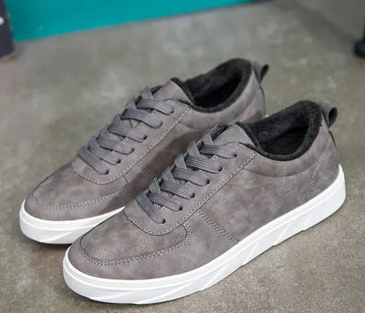 Pair of gray sneakers with white soles on a concrete floor.