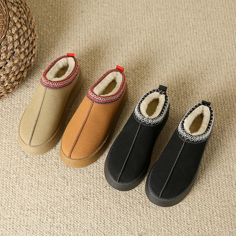 Four pairs of slippers in beige, brown, black, and another black color on a textured surface.