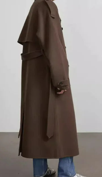 Person wearing a long brown coat with a plain background
