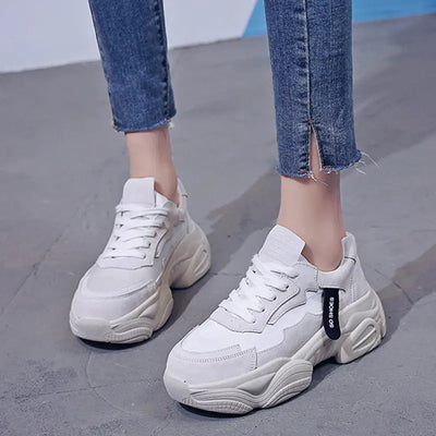 White sneakers worn with blue jeans on a gray pavement.