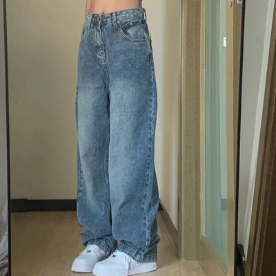 Person wearing blue jeans and white sneakers in a room with a neutral wall and wooden floor.