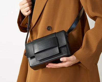 Person holding a black handbag with a plain background