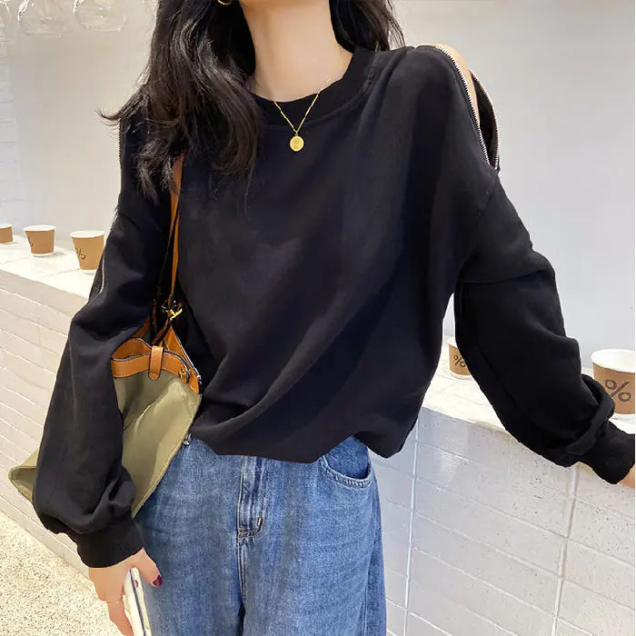 Person wearing a black sweatshirt and blue jeans holding a green bag indoors.