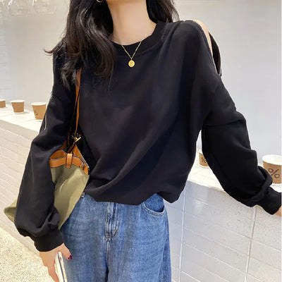 Person wearing a black sweatshirt and blue jeans holding a green bag indoors.