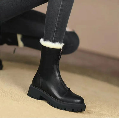 Black ankle boot with white fur lining worn by a person on a beige floor.