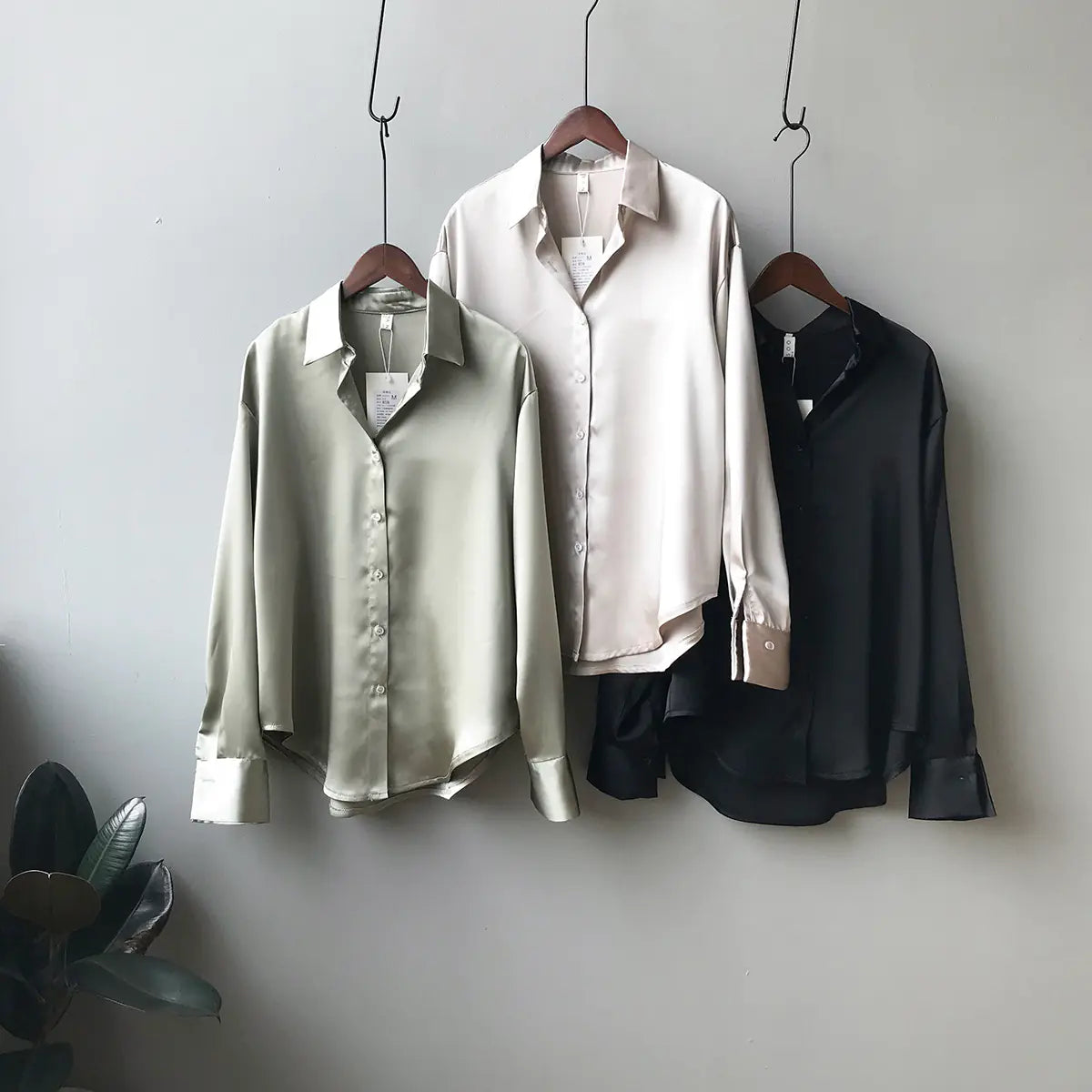 Three shirts in green, white, and black hanging on a gray wall.