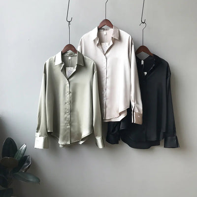 Three shirts in green, white, and black hanging on a gray wall.