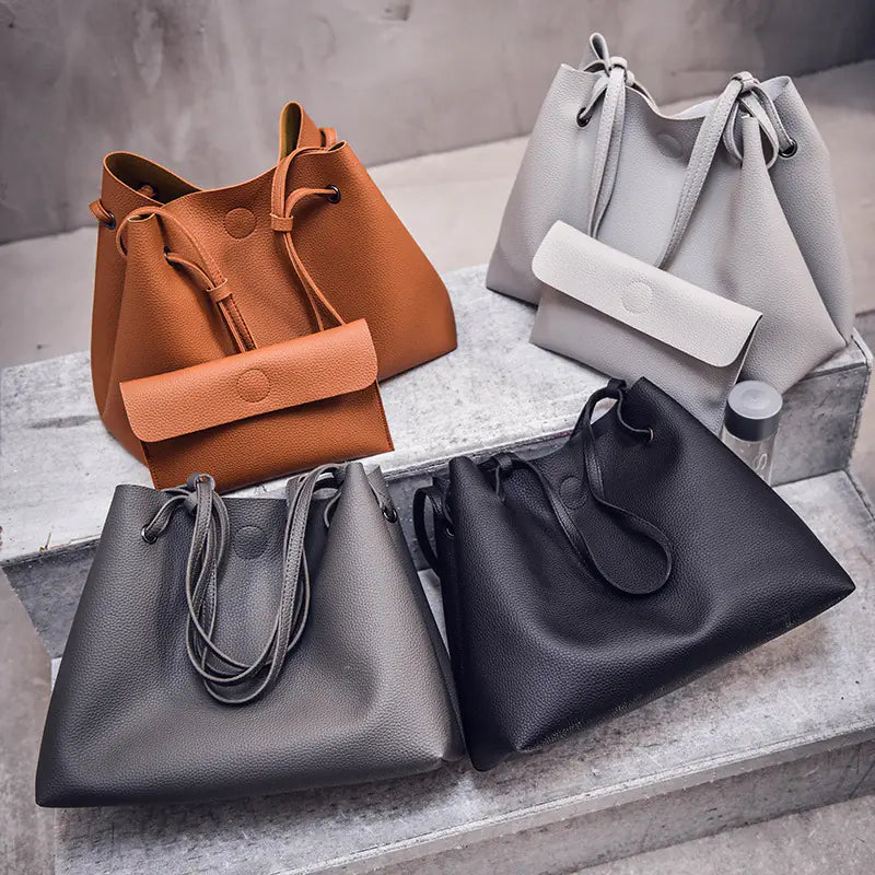Four handbags in brown, gray, and black on a concrete surface.