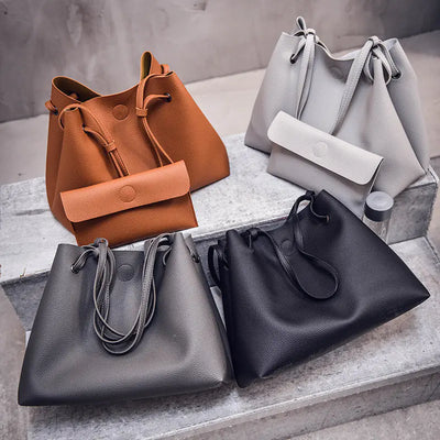Four handbags in brown, gray, and black on a concrete surface.