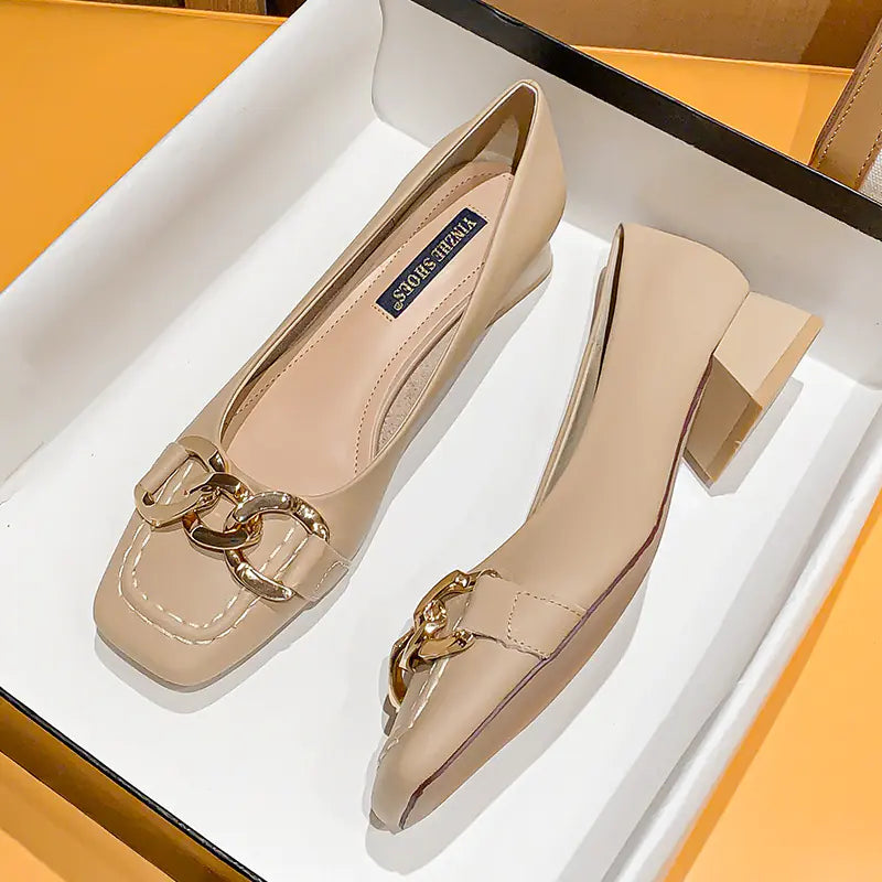 Pair of beige shoes with gold chain detail on a white and orange background