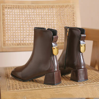 Pair of brown ankle boots with gold buckles on a woven surface