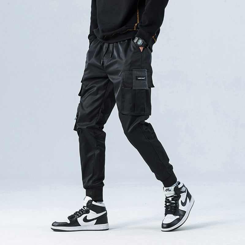 Person wearing black cargo pants and black and white sneakers on a light gray background