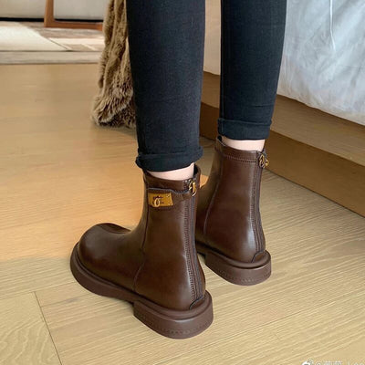 Brown leather boots worn with black pants on a wooden floor.