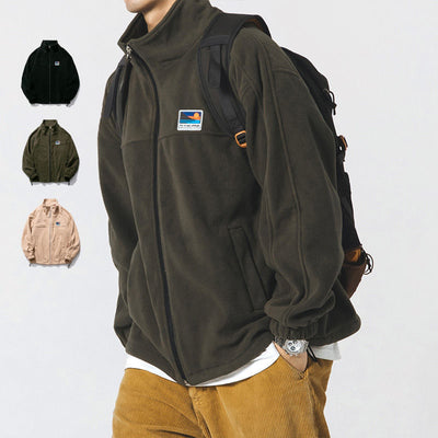 Person wearing a dark green jacket with a brand logo, standing against a white background.