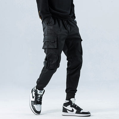 Person wearing black cargo pants and black and white sneakers on a light gray background