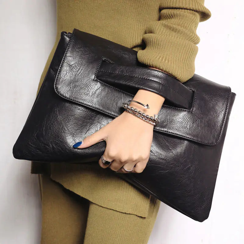 Person holding a black leather clutch bag with a plain background