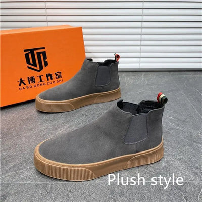 Gray Chelsea boots with brown soles in front of an orange box with branding on a gray floor.