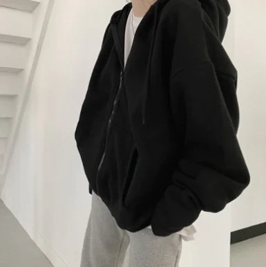 Person wearing a black hoodie and light gray pants in a minimalistic setting
