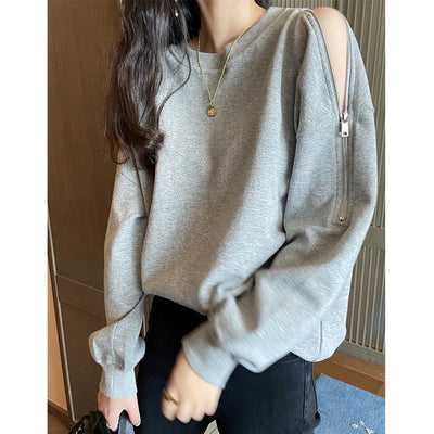 Person wearing a gray sweater with a zipper detail, standing indoors.
