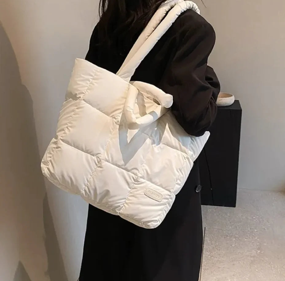 Person holding a white puffer bag against a neutral background