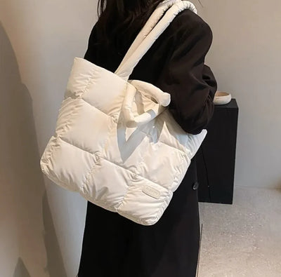 Person holding a white puffer bag against a neutral background