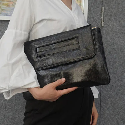 Person holding a black clutch bag against a gray background