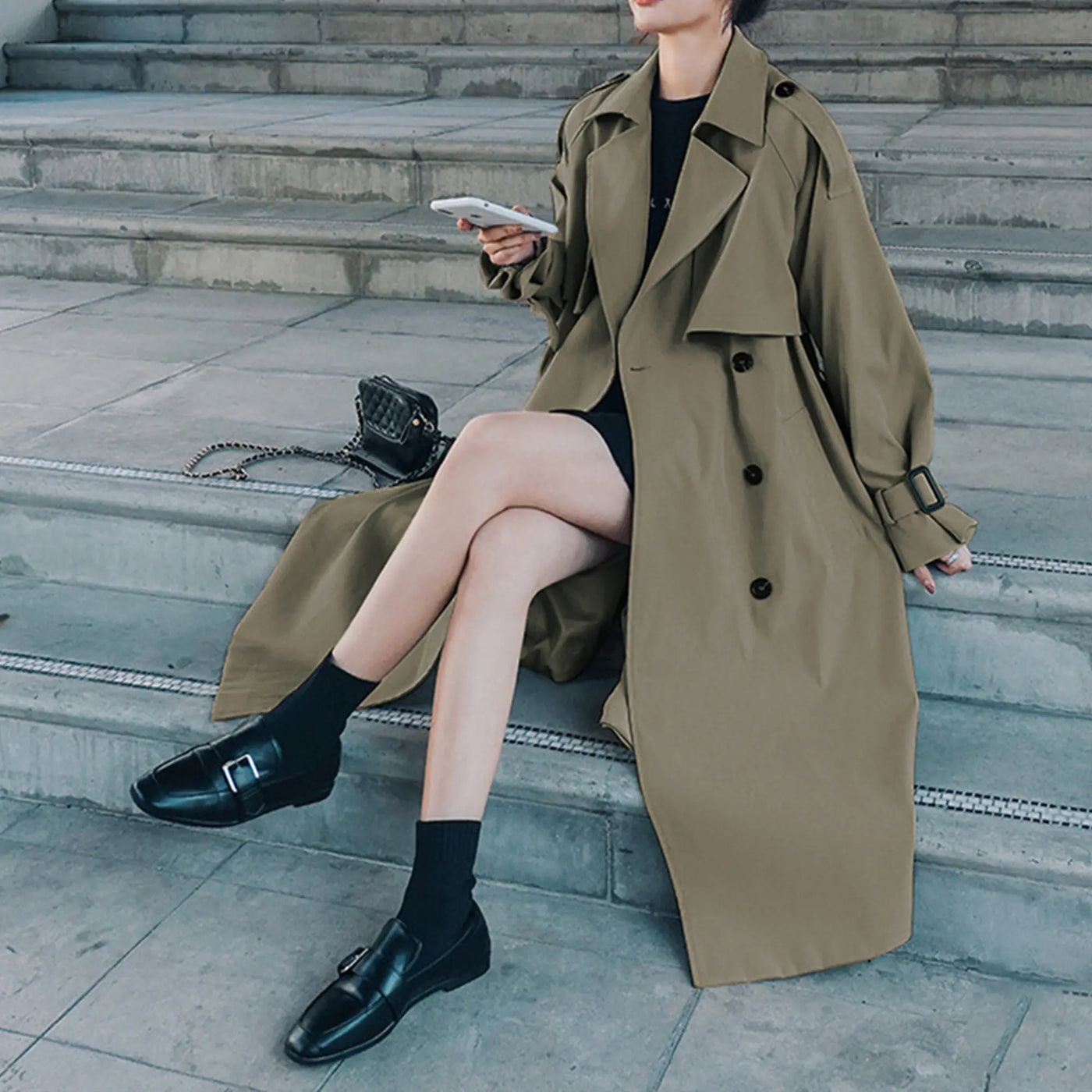 Person wearing a long beige trench coat sitting on steps.