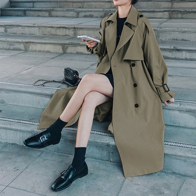 Person wearing a long beige trench coat sitting on steps.