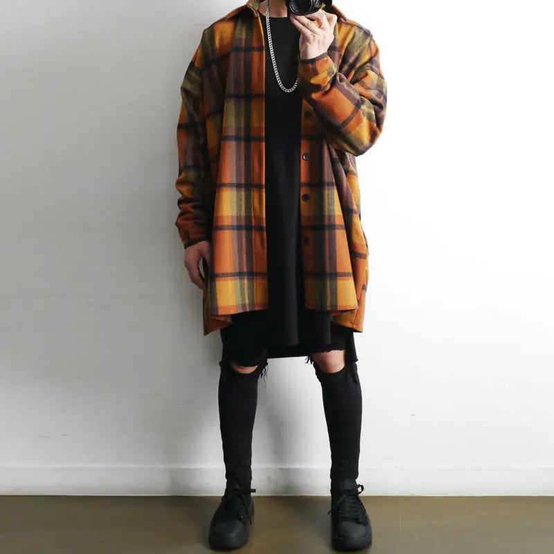 Person wearing a plaid coat over a black outfit with knee-high socks against a plain background