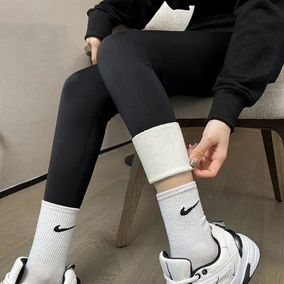 Person wearing black leggings and white socks with a brand logo, sitting on a chair.