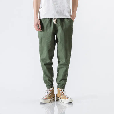 Person wearing green jogger pants and beige high-top sneakers on a white background