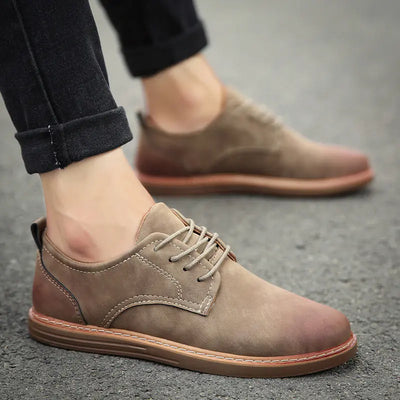 Brown suede shoes worn with black pants on a gray pavement.
