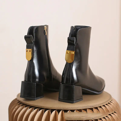 Black ankle boots with gold accents on a beige surface
