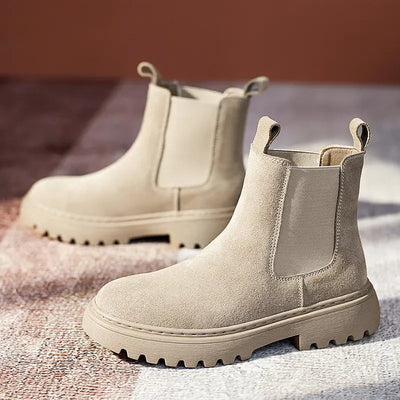 Pair of beige Chelsea boots on a textured surface with a blurred background