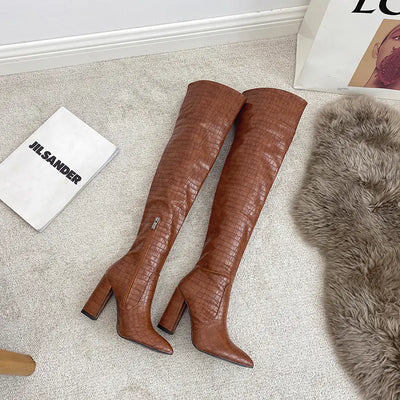 Brown knee-high boots on a light gray carpet with a Jil Sander bag in the background.