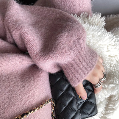 Person wearing a pink textured sweater holding a black quilted handbag.