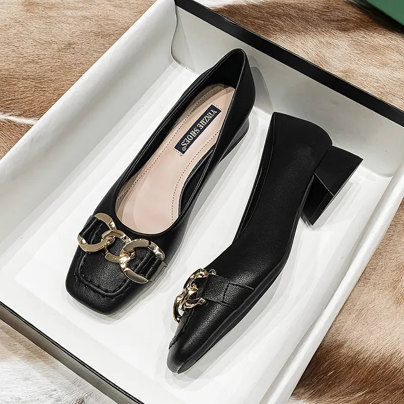 Black shoes with gold chain detail on a white box