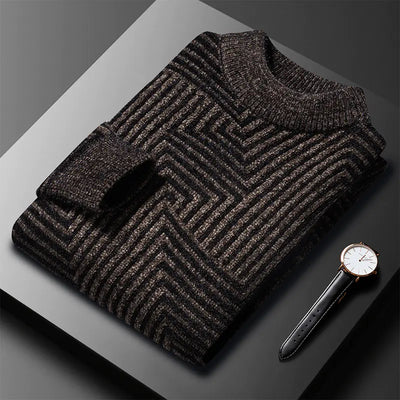 Folded black patterned sweater on a gray surface with a watch beside it