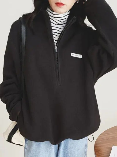 Person wearing a black half-zip sweatshirt with a brand logo on a light background