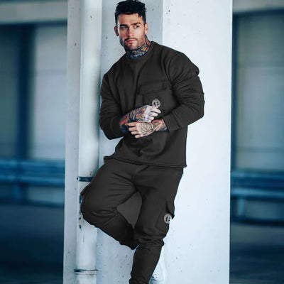 Man in black tracksuit leaning against a white column with tattoos visible